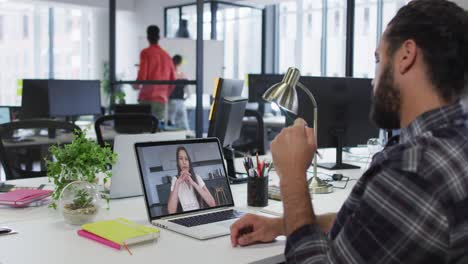 hombre de negocios de raza mixta sentado en un escritorio usando una computadora portátil haciendo una videollamada con una colega