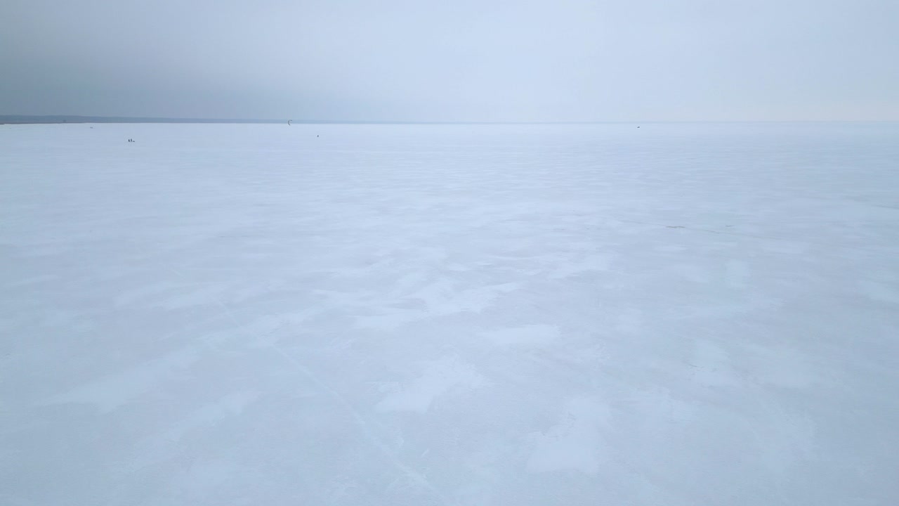 Monochromatic flight low over frozen sea ice with grey sky horizon