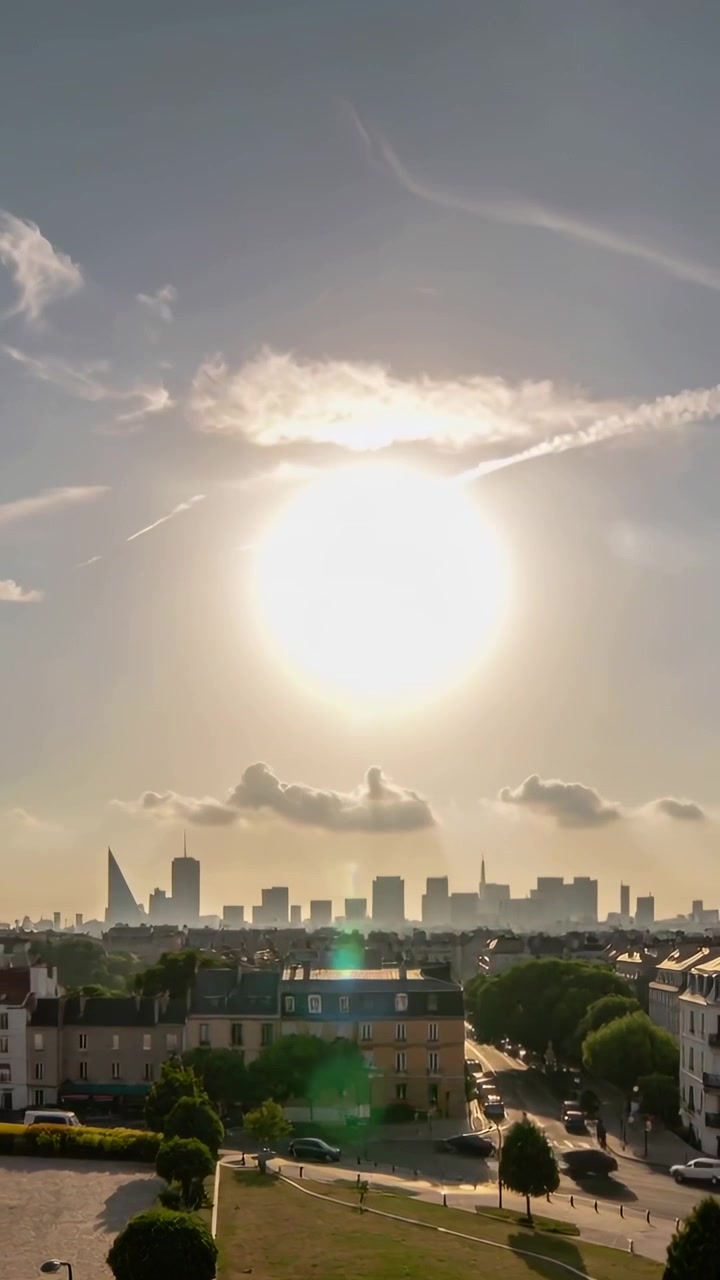 Vídeo vertical: Sol brilhante criando reflexo de lente verde e iluminando telhados, parque triangular, horizonte.