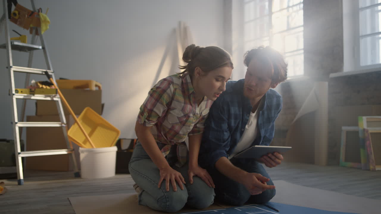 Koppel bestudeert plan op de vloer. Familie maakt woningrenovatieplannen op tablet.