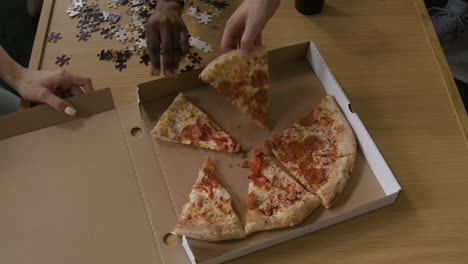 hands taking slices of pizza from a box during a puzzle session