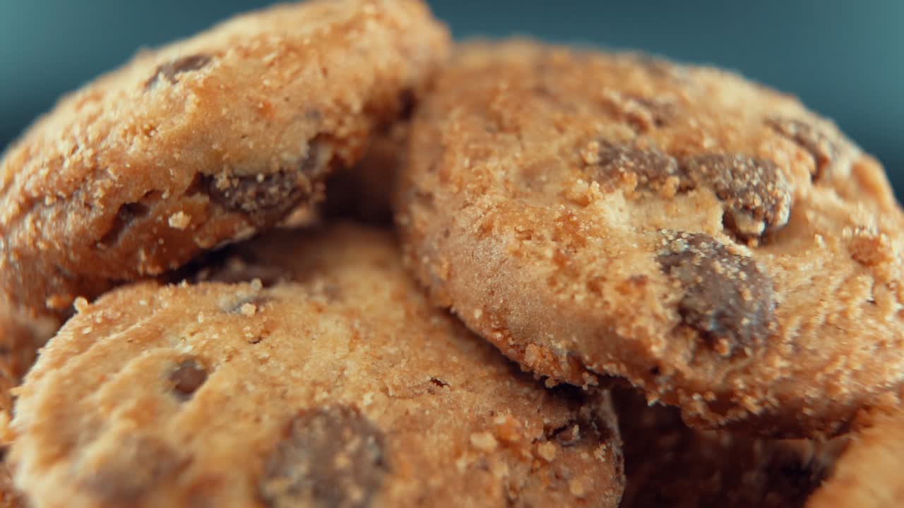 A macro close up cinematic shot of a plate full of crispy chocolate chip cookies, on a rotating stand, studio lighting, super slow motion, 120 fps, Full HD