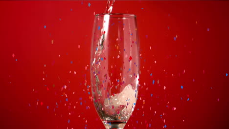 animation of multi coloured confetti falling over champagne flute on red