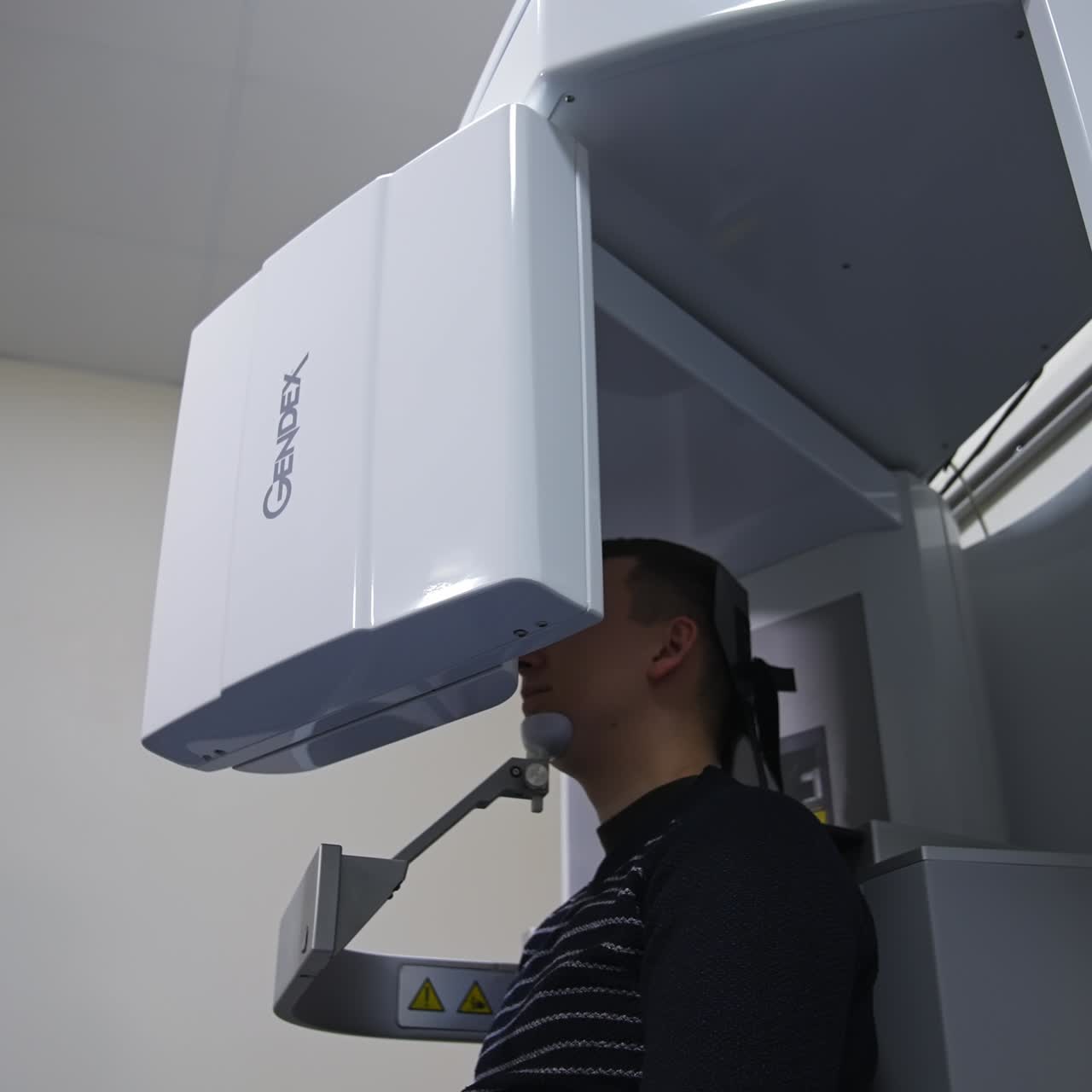 Male patient sitting in the apparatus taking an x-ray shot of teeth. Advanced equipment in modern dentist clinic. Low angle view
