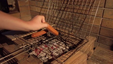 handheld shot of man placing sausages into a grilling basket on a charcoal bbq at night