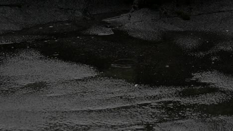 rain drops are falling down on water puddle on asphalt and making moody and sad mood