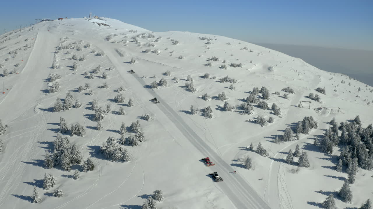 Snowcats grooming a ski slope on a snowy mountain