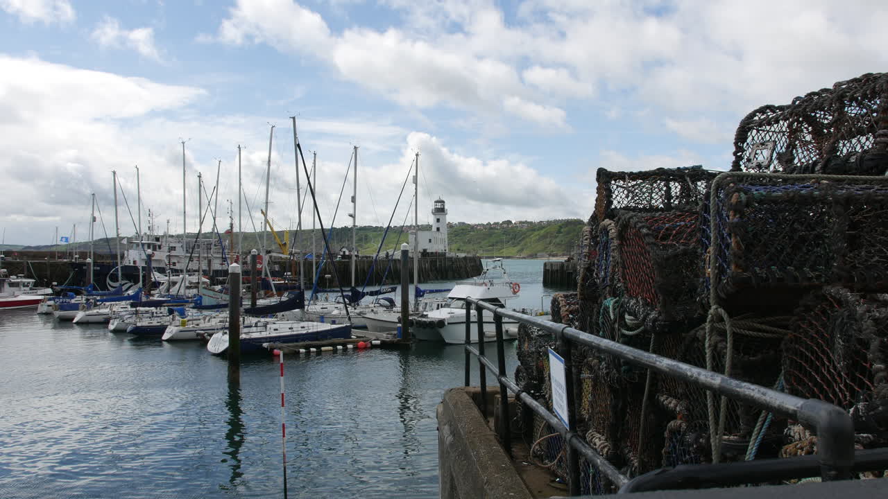 Fishing nets and ropes stacked on the harbor edge in Scarborough, North Yorkshire in England, with boats docked nearby and a lighthouse across the calm water