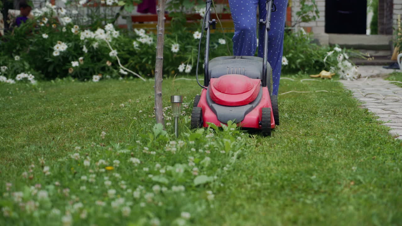 woman cutting grass in his yard with corded electric lawn mower.