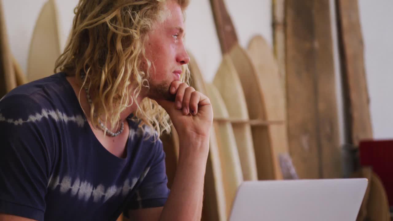 Caucasian male surfboard maker working on a project using his laptop