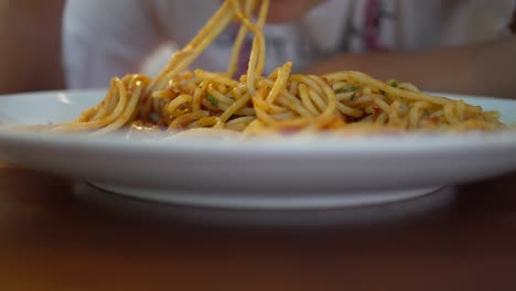 a little girl eats tomato seafood spaghetti in a restaurant. the subject is in the middle of the screen.