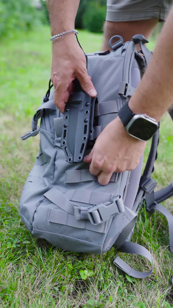 Vertical shot - male attach holster with knife on camping backpack, Czechia