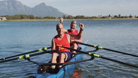 two senior caucasian men in rowing boat raising hands and cheering