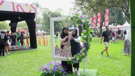 asian women in hijab posing with hand heart in decorated photo booth at bogor botanical gardens, indonesia. wide shot