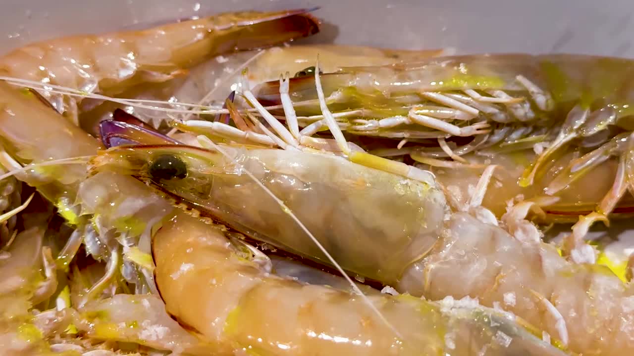 Close-up of a hand seasoning fresh prawns with salt, highlighting the texture and preparation process.