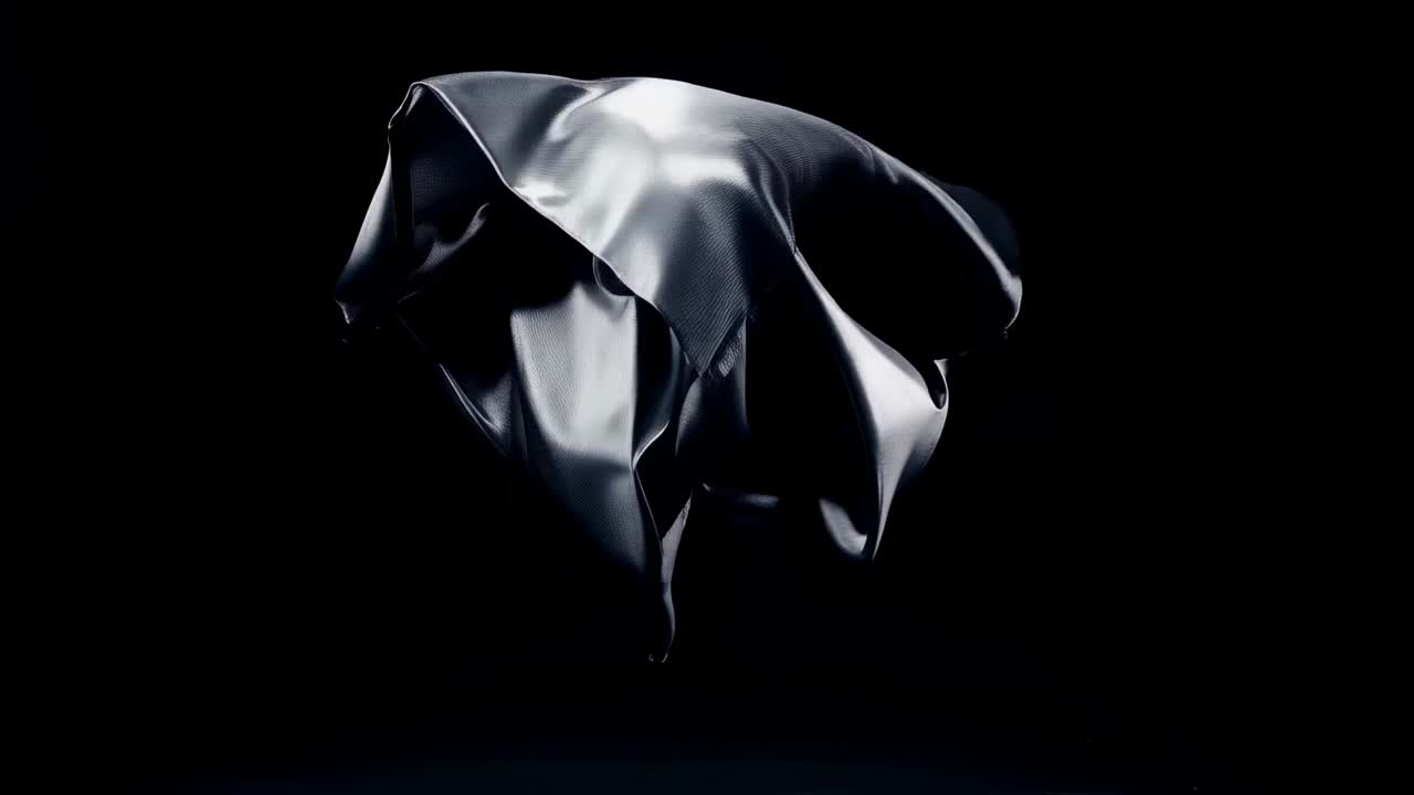 After release descending metallic sheet unfurling crumpling and rotating in studio spotlights