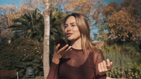 una mujer hermosa y alegre grabando un mensaje de voz al aire libre.