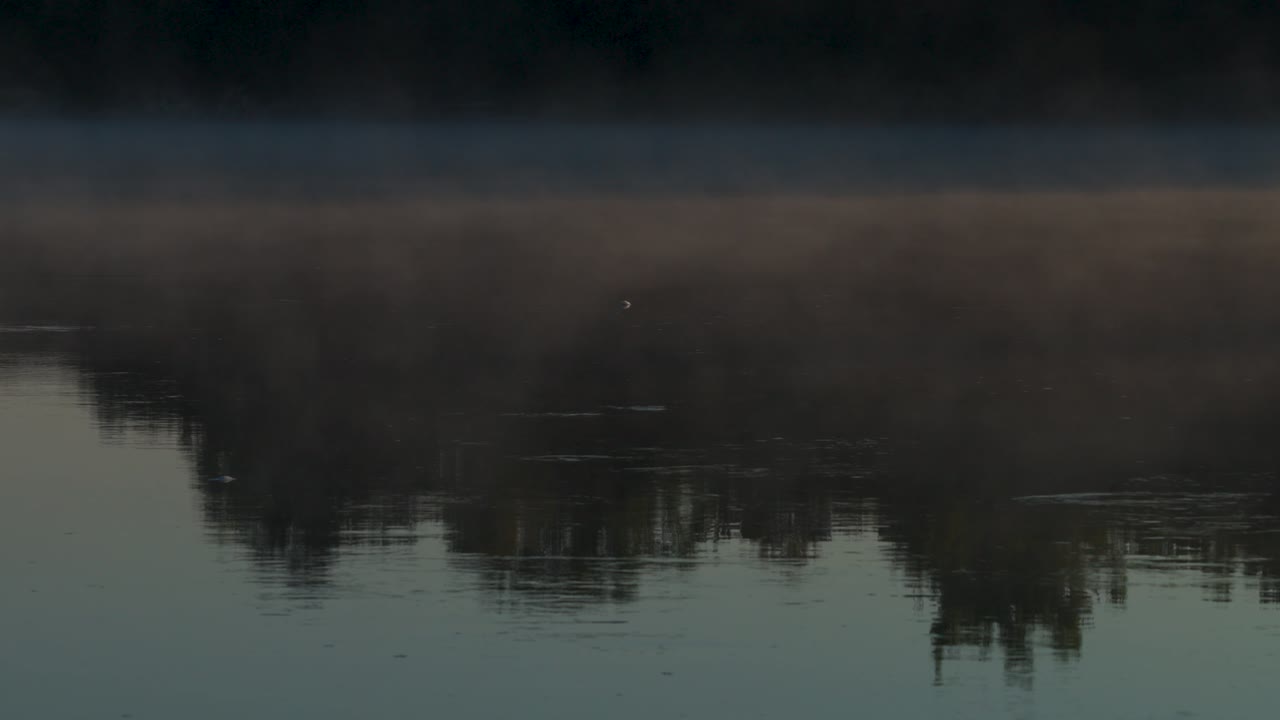 A view of a calm stretch of water on the Gatineau River with morning mist rising