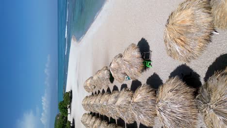 Cozy-straw-parasols-on-white-sand-beach,-luxury-holiday-resort,-aerial-portrait