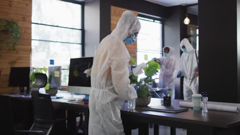 equipo de trabajadores de la salud con ropa de protección limpiando la oficina con un pulverizador de desinfectante