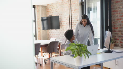 collaborating on project, two businesswomen using laptop in modern office space