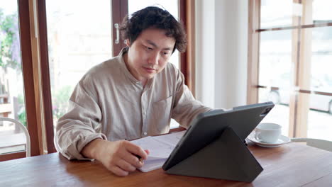 adult man sit and take note for online studying with tablet in cafe during daytime