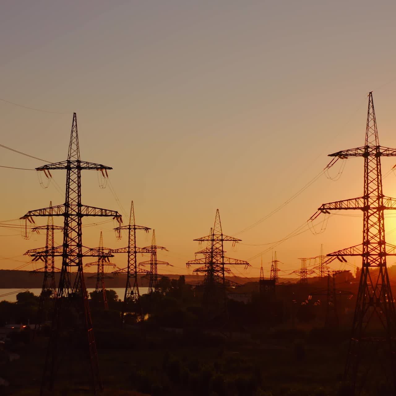 High voltage electrical lines at sunset. Dark silhouette of towers in the rays of the beautiful evening sun. Distribution and supply of electricity. Camera moves back.