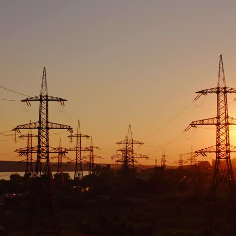 high voltage electrical lines at sunset. dark silhouette of towers in the rays of the beautiful evening sun. distribution and supply of electricity. camera moves back.