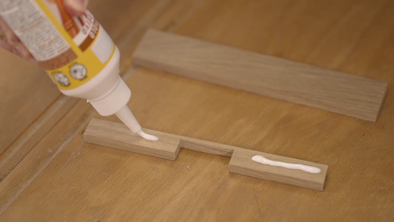 Video close-up pengaplikasian lem kayu ke sambungan kayu selama pengerjaan kayu. Proses pertukangan DIY, produksi furnitur buatan tangan, dan pekerjaan perakitan yang presisi.
