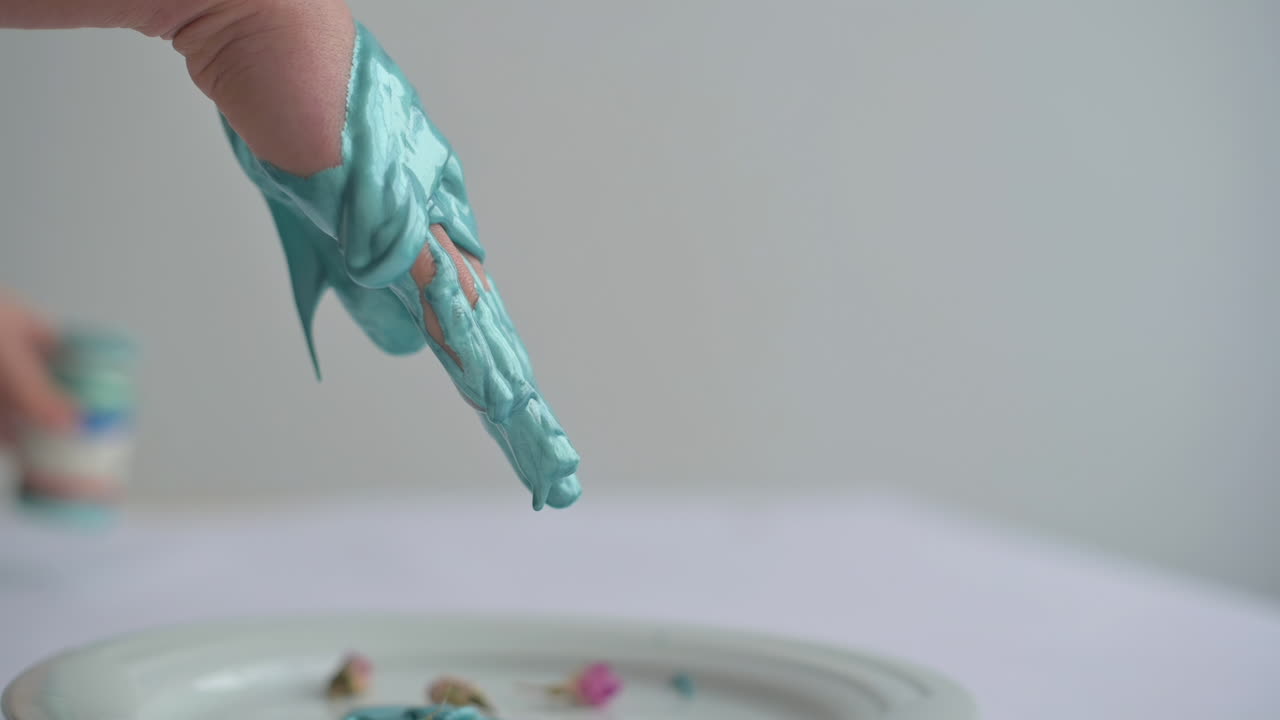 A child joyfully explores a hand painting activity using blue paint, creating art with flowers on a white plate, showcasing fun creativity indoors