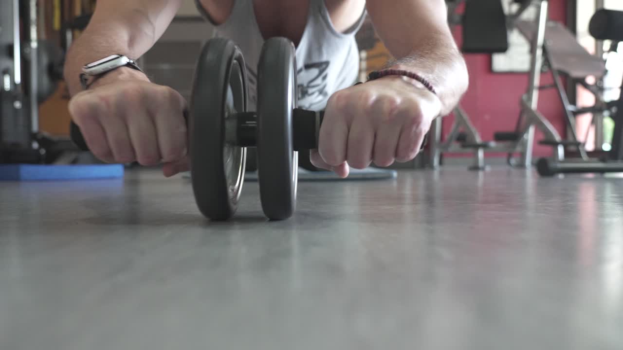 A man performing an ab wheel rollout exercise in a gym. This movement emphasizes core strength, stability, and endurance, showcasing the concept of functional training and fitness improvement.