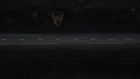 A-Birds-Eye-view-of-an-isolated,-long-road-in-the-South-of-Iceland-surrounded-by-black-sand,-aerial