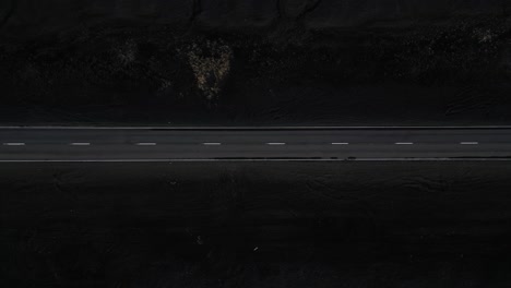 a birds eye view of an isolated, long road in the south of iceland surrounded by black sand, aerial