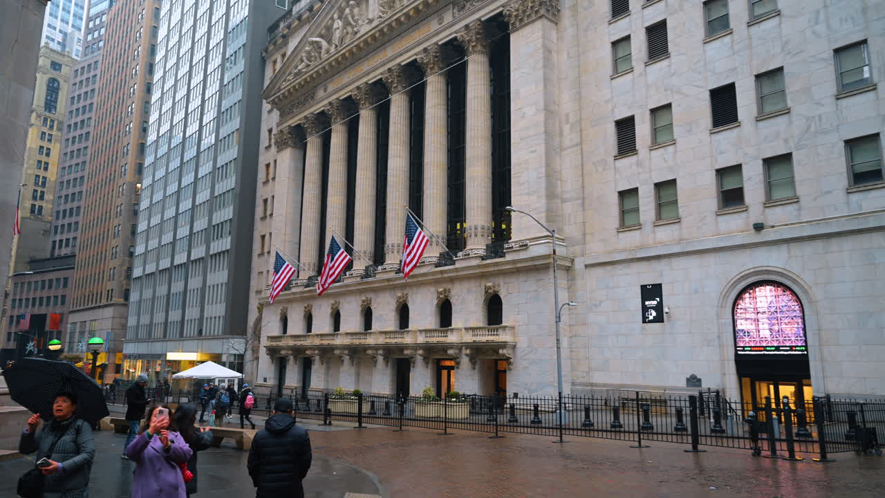 New York, USA, 28. december 2025: Folk samles uden for New York Stock Exchange på en regnvejrsdag i byen. Folk står nær New York Stock Exchange i let regn, mens de holder paraplyer og tager billeder