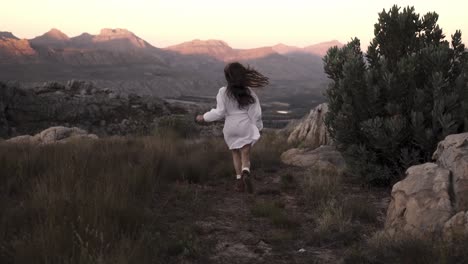 Mujer-Irreconocible-Corriendo-Hacia-La-Cordillera-En-Un-Entorno-Rocoso,-Libertad-En-Cámara-Lenta-Y-Escena-De-Aventura-Vista-Desde-Atrás