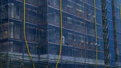 close up view of a construction site where workers are working in asbestos suits within blue safety net