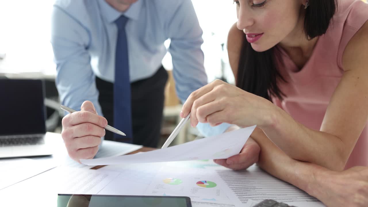 Two business professionals discuss financial documents and data in an office
