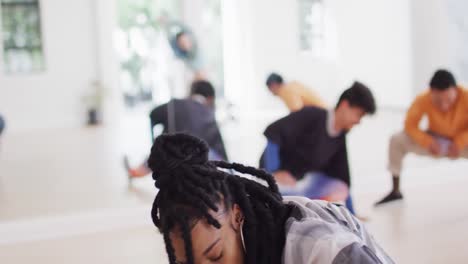 Biracial-female-dancer-stretching-with-diverse-colleagues-in-dance-studio,-slow-motion