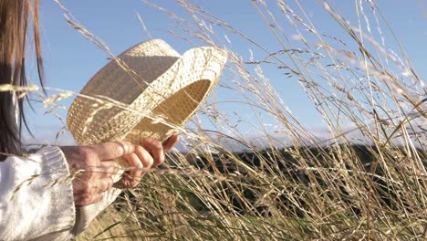 Woman-holding-straw-hat-in-tall-grass-medium-shot