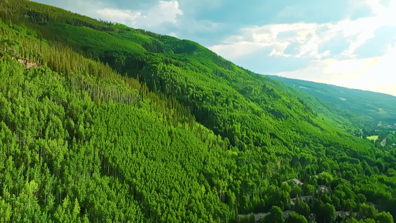 Drone approach pan of ridged hillside in Vail with deep green vegetation under clear summer skies