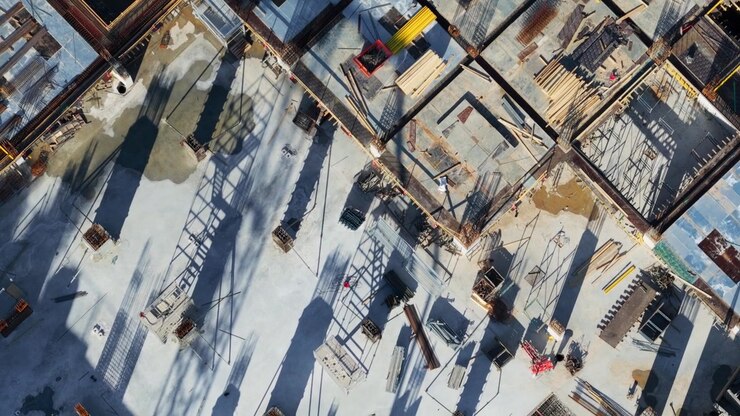 Top-down aerial view capturing the various stages of building construction, showcasing the architectural grid, foundation work, concrete pouring, and progression from the ground floor up