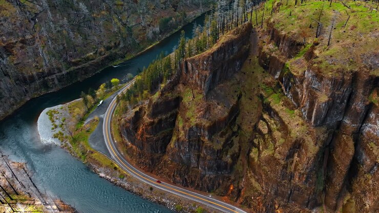 Spectacular bare rocks with rare pine trees growing on top. Narrow river flowing at the foot of the mountain and highway is built around the mount. Top view.
