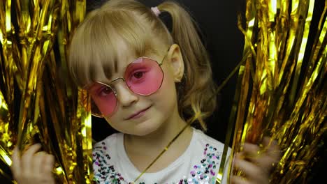 portrait of happy child playing, fooling around in foil fringe golden curtain. little blonde kid