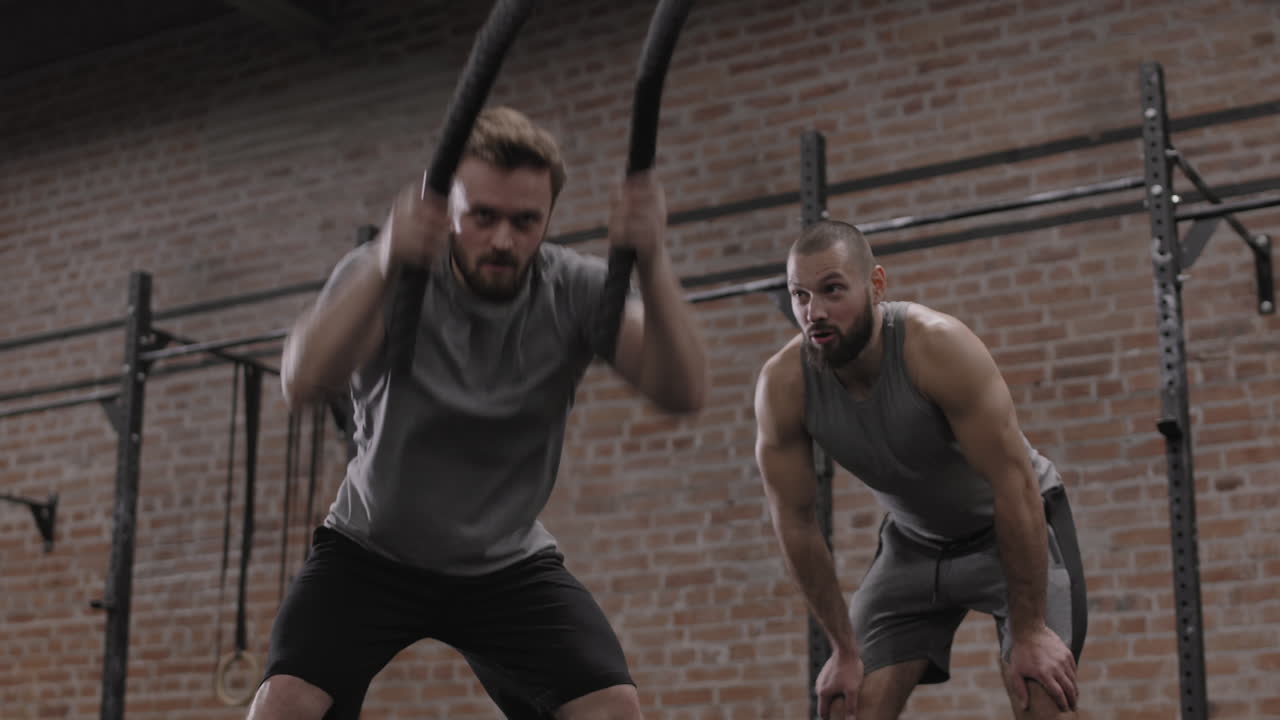 Coach Controlling Young Sportsman Exercising with Battle Ropes