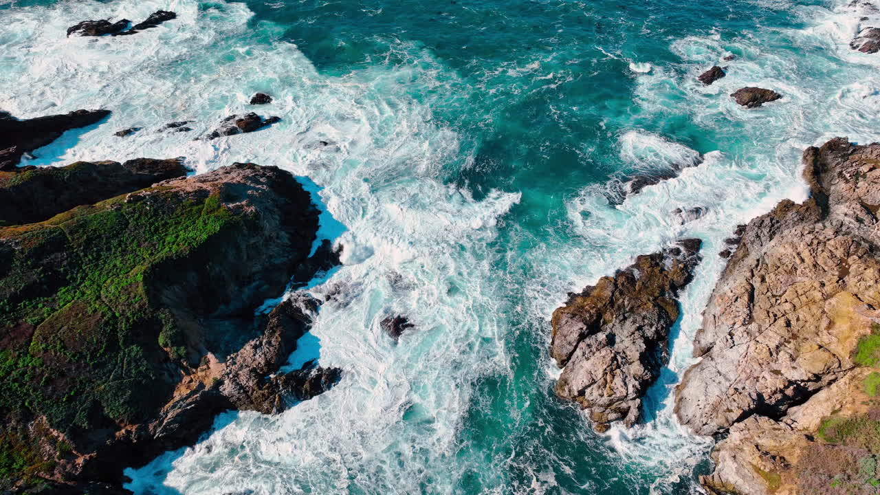 Vista dall'alto di un'insenatura rocciosa con onde che si infrangono. Ripresa aerea di un'insenatura oceanica con vegetazione verde su scogliere rocciose e spuma bianca a Big Sur, California.