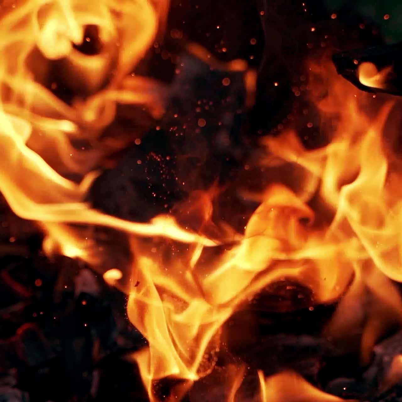 Bright sparkles flying from the fire at night. Wooden stick break smoldered logs in fire and flame becomes brightly outdoors. Slow motion.