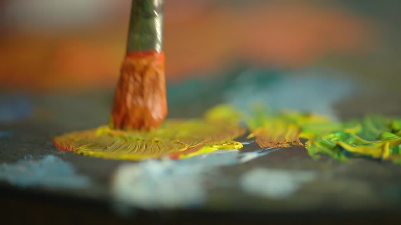 Primo piano di un pennello che mescola pittura gialla e arancione su una palette