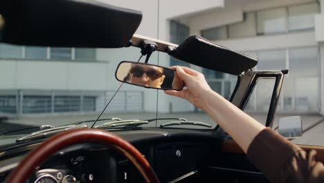 woman adjusting rearview mirror in classic convertible car