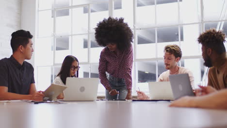 Millennial-black-female-manager-stands-addressing-coworkers-sitting-in-a-meeting-room,-close-up