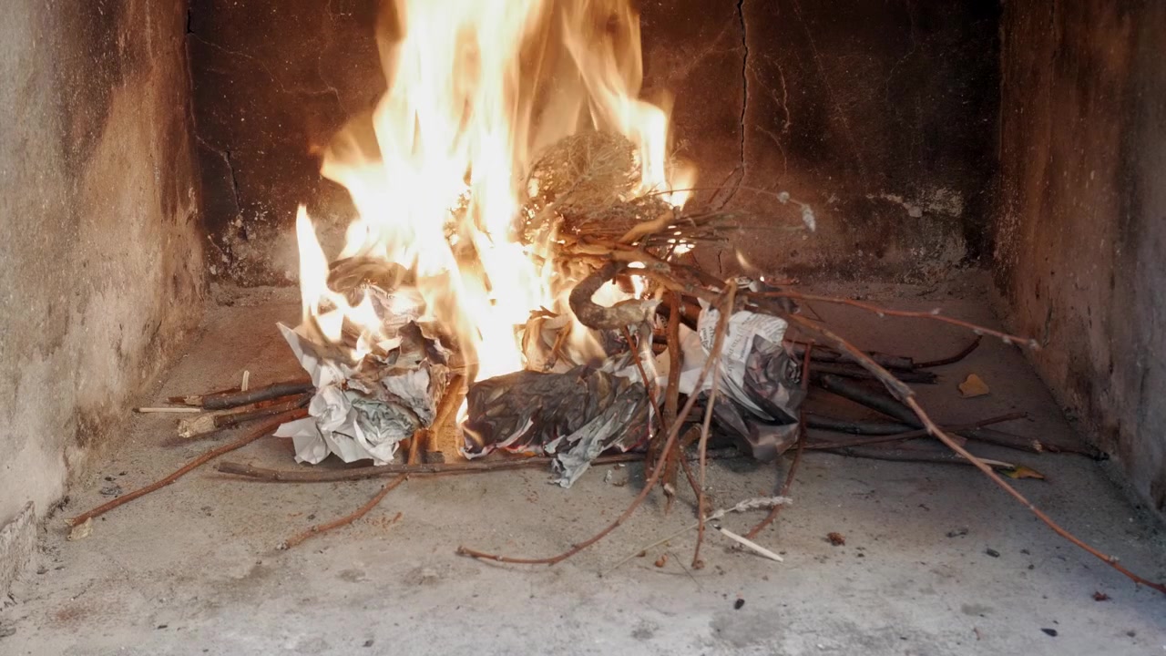 Hand arranges sticks and paper as a fire grows in an indoor fireplace or oven